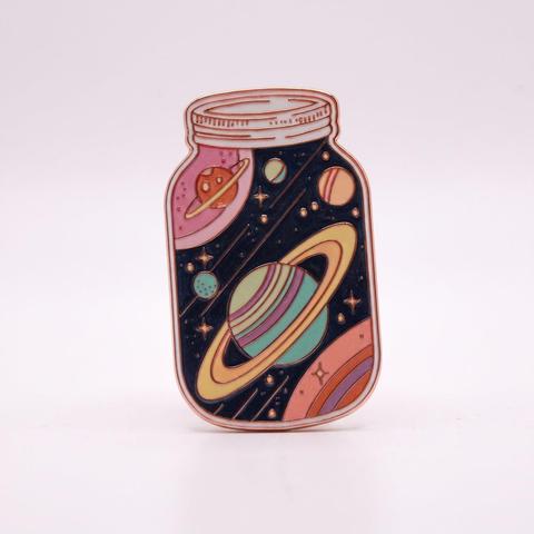 An enamel pin shaped like a glass mason jar containing colorful planets, stars, and outer space.