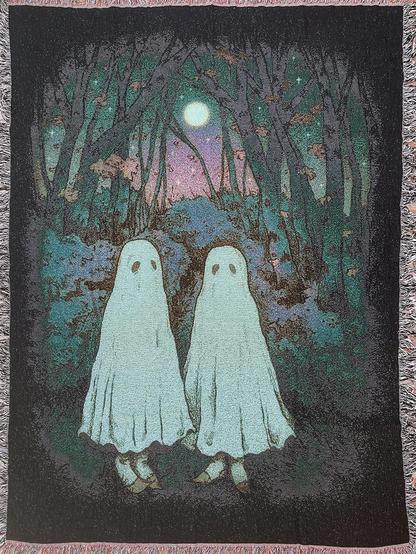 ​A woven blanket illustration featuring two white sheet ghosts standing side-by-side in a dark, twilight forest under a full moon.