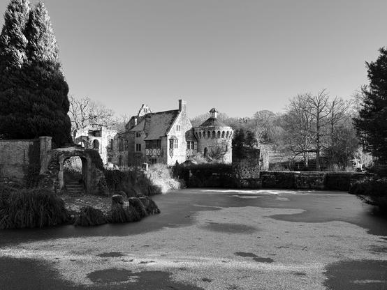 Black and white image of Scotney Castle showing the tower and house across the frozen moat.