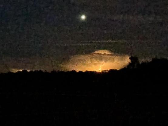 Dark night photo with horizon across middle of image with bright orange lightning showing up a cloud 140 miles away.