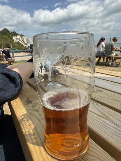 Pint of MasterBrew on a wooden table at the Coastguards pub in Stmargarets bay. You can see the white cliffs behinde the pintand the sea to the right